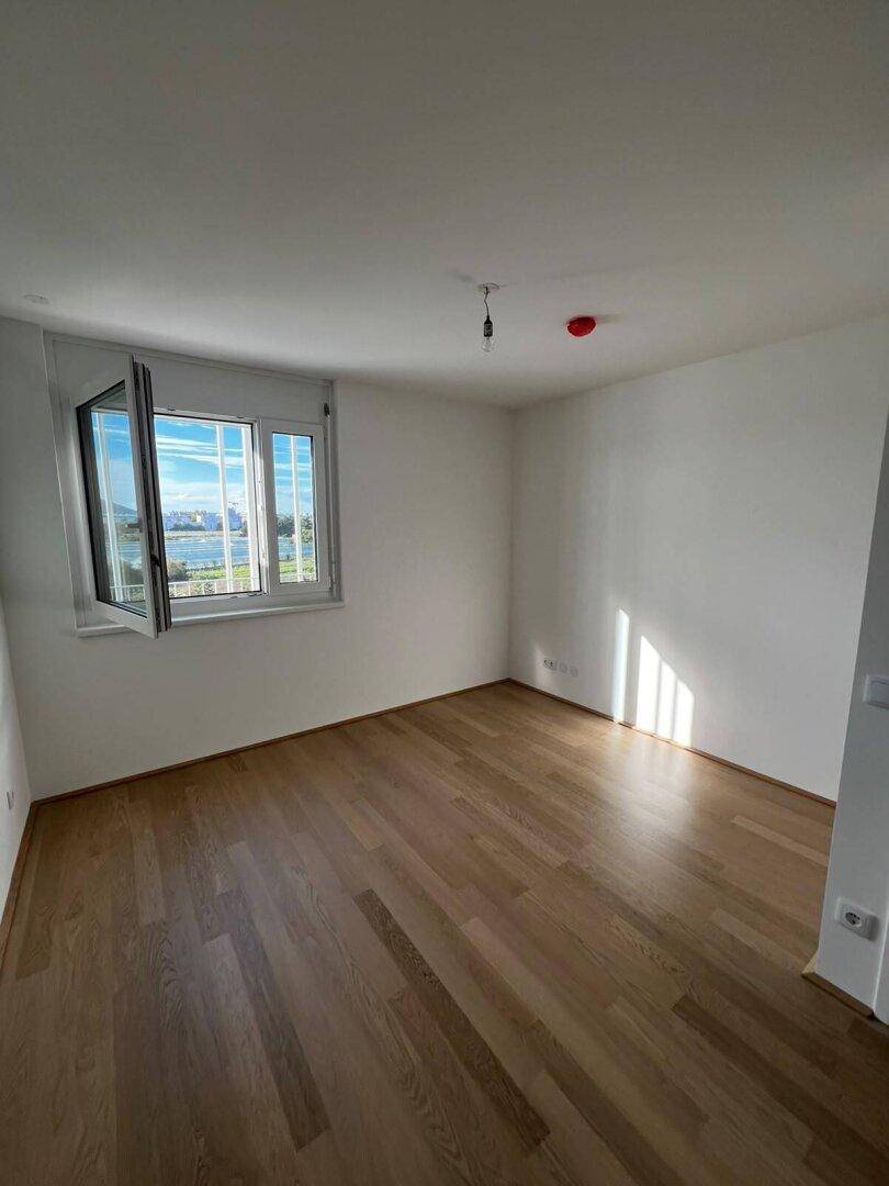 Helles Schlafzimmer mit hellem Holzfußboden und einem Fenster, das einen weiten Blick auf die Umgebung bietet.