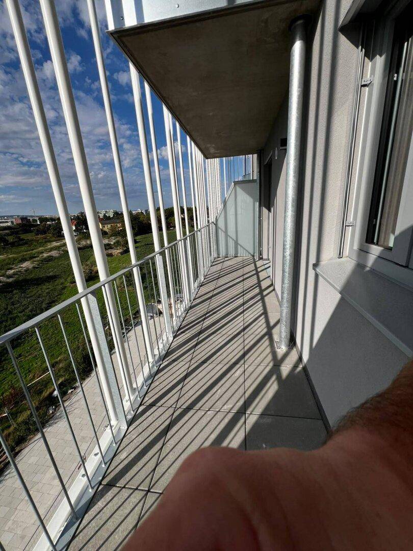 Langer Balkon mit moderner Metallbrüstung und weitem Blick über die grüne Landschaft unter blauem Himmel.