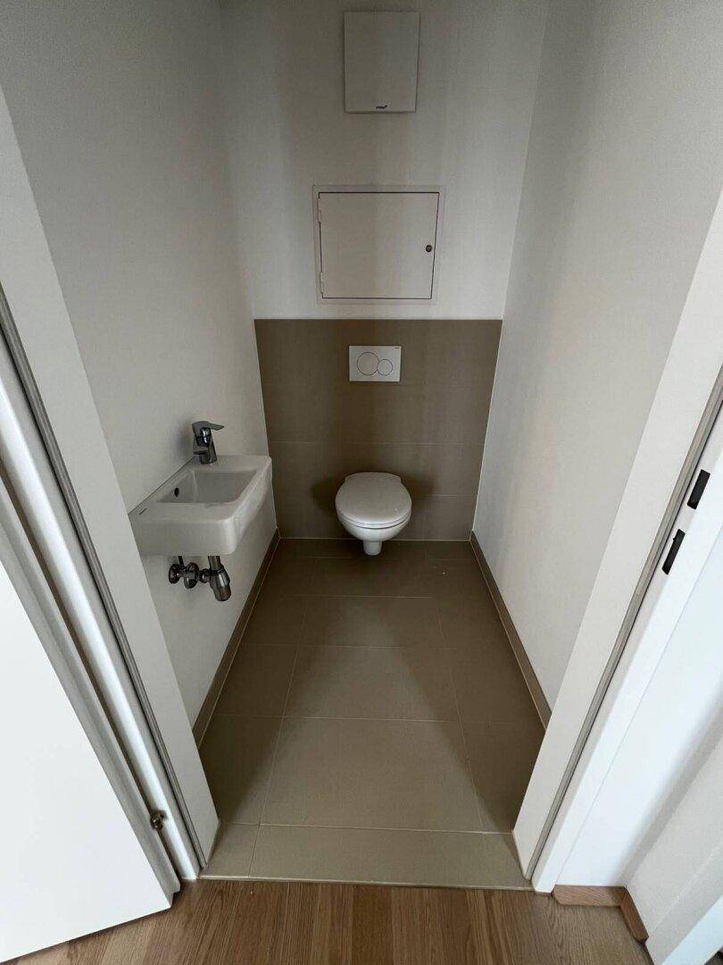 Modernes Gäste-WC mit wandhängender Toilette, kleinem Waschbecken und hellen Fliesen an Boden und Wänden.