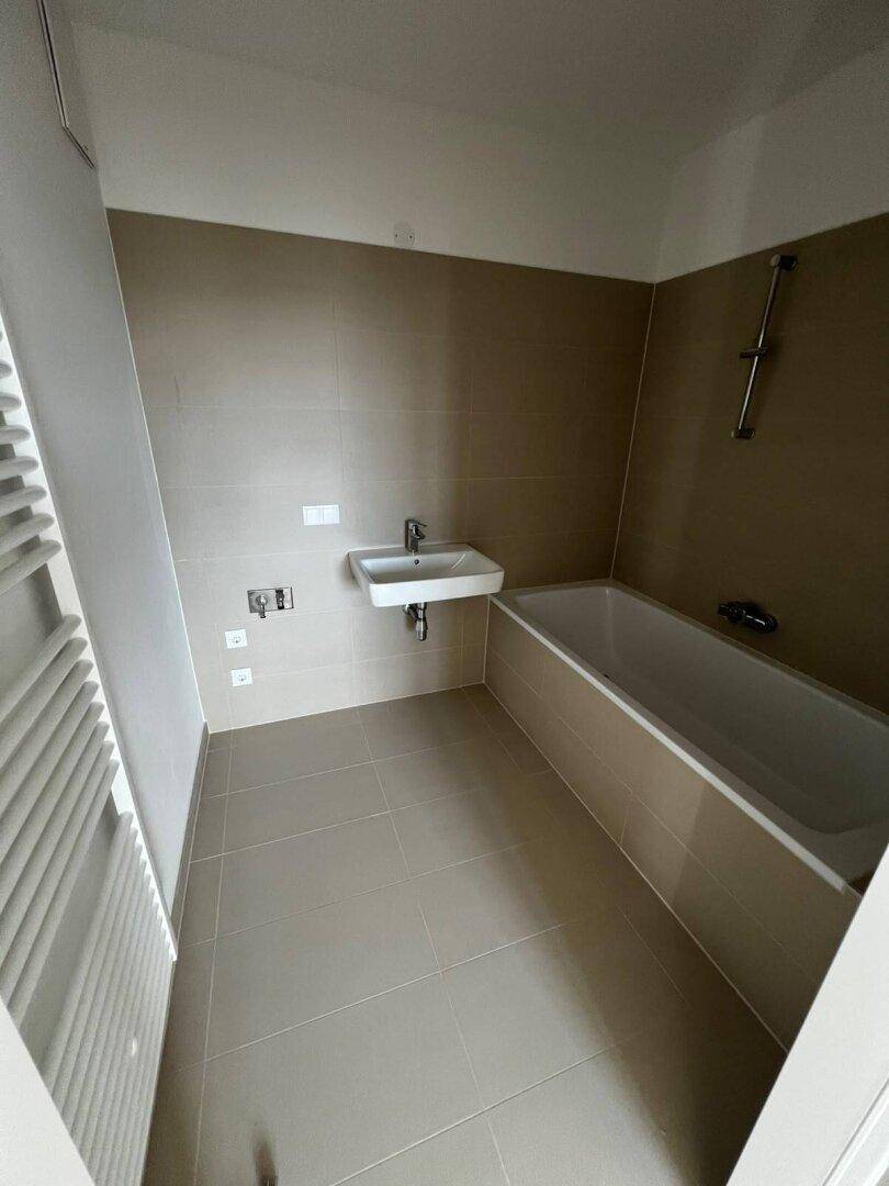 Modernes Badezimmer mit Badewanne, Waschbecken und beheiztem Handtuchhalter, komplett gefliest.