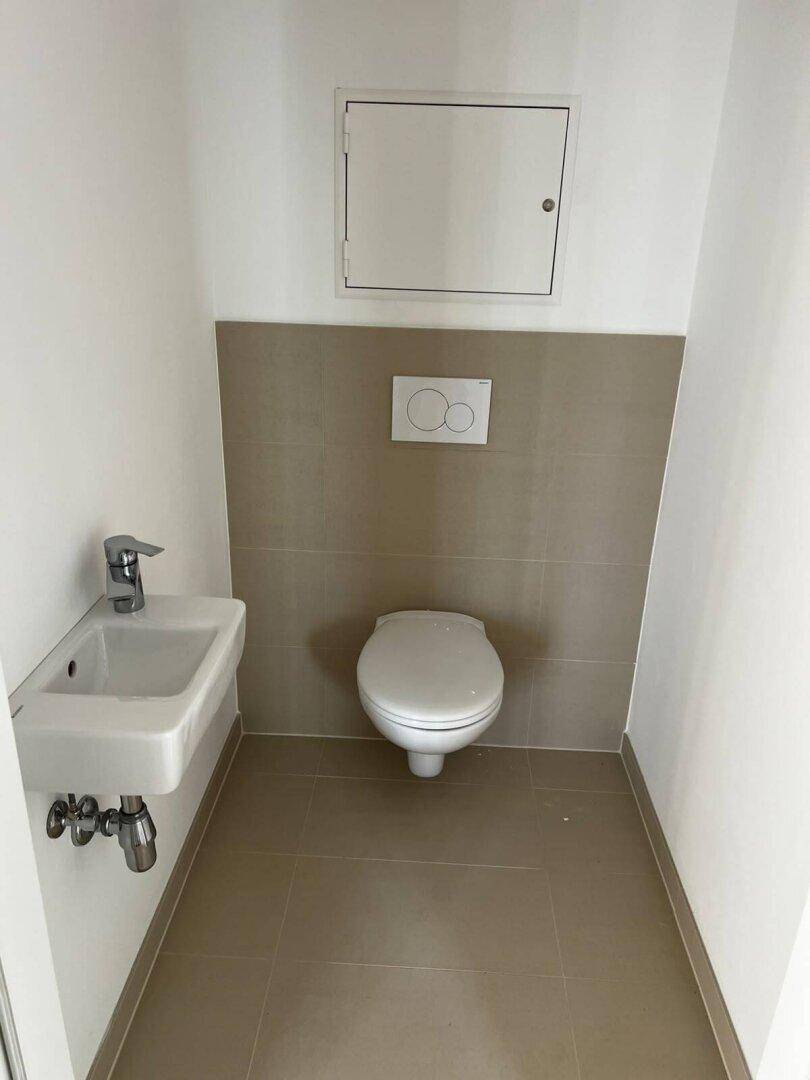 Sauberes Gäste-WC mit wandhängender Toilette und kleinem Waschbecken, ausgestattet mit hellen Fliesen.