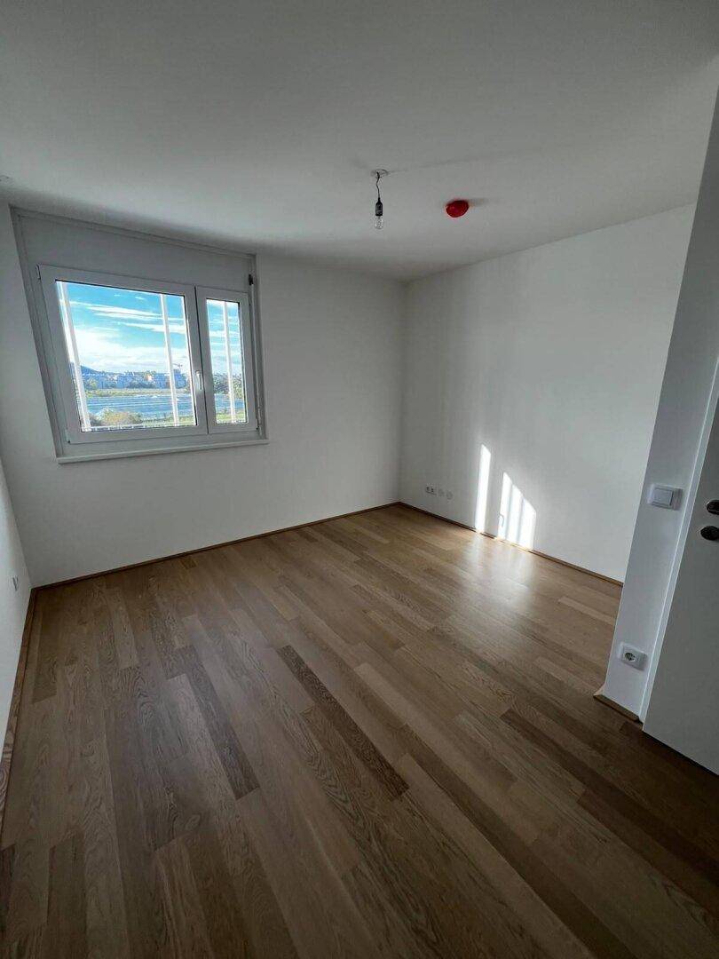 Helles Schlafzimmer mit hellem Holzfußboden und einem Fenster, das einen weiten Blick auf die Umgebung bietet.