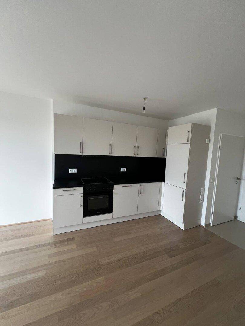 Moderne Einbauküche mit weißen Schränken, schwarzer Arbeitsplatte und hellem Holzfußboden in einem leeren Raum.