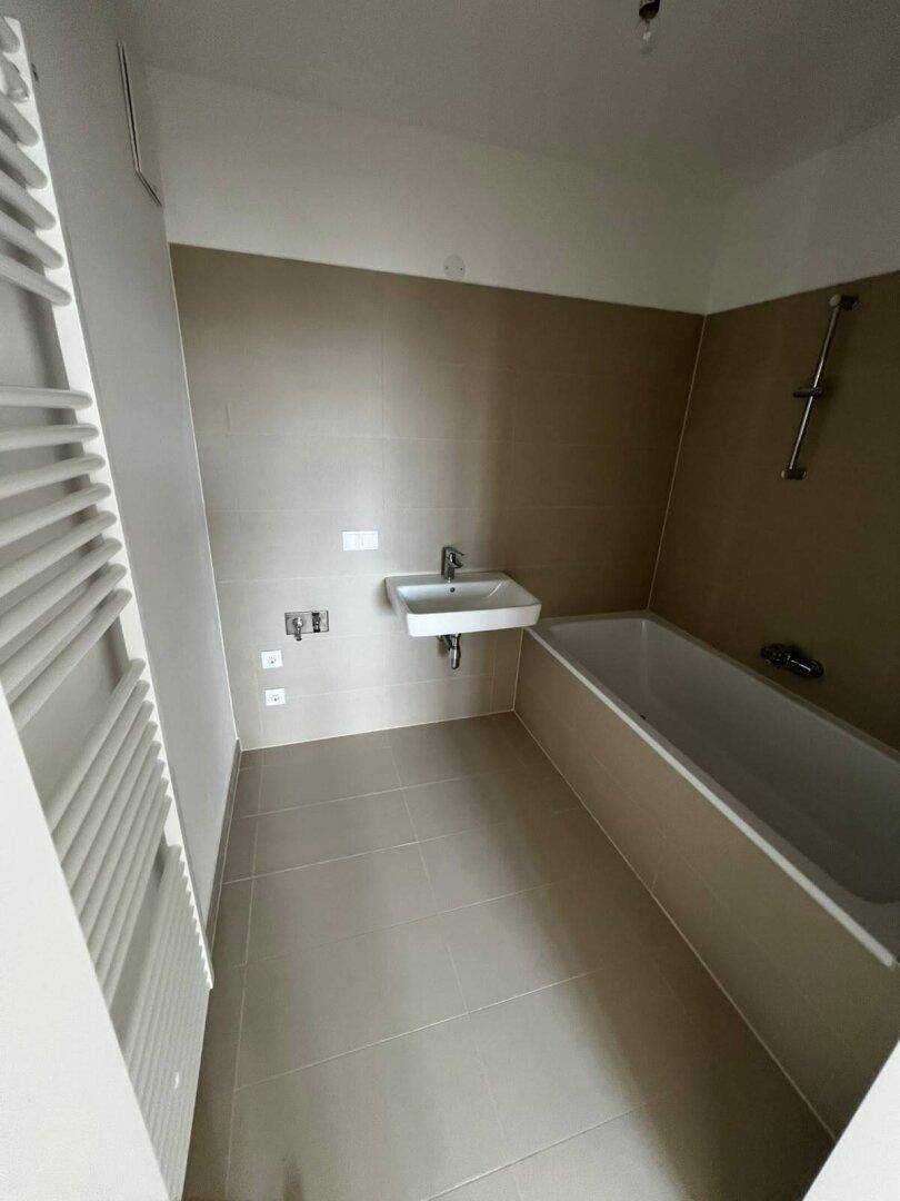 Modernes Badezimmer mit Badewanne, Waschbecken und beheiztem Handtuchhalter, komplett gefliest.