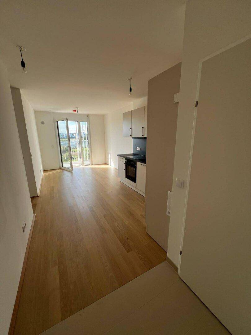 Heller Wohnbereich mit hellem Holzfußboden, integrierter Küchenzeile und Zugang zu einem sonnigen Balkon.