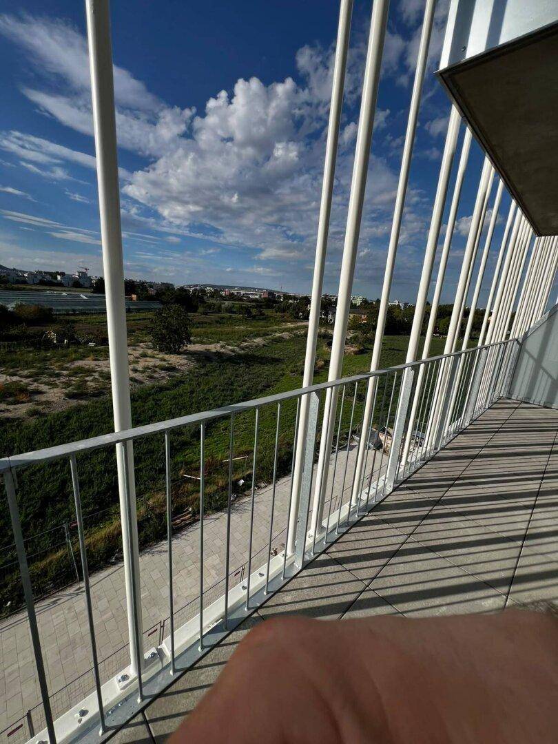 Sonniger Balkon mit Blick auf weite Felder und den Horizont, umgeben von einer modernen Gebäudestruktur.