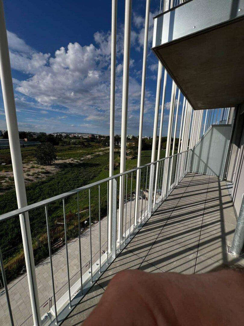 Geräumiger Balkon mit moderner Brüstung und freiem Blick auf die umliegende Natur und den blauen Himmel.