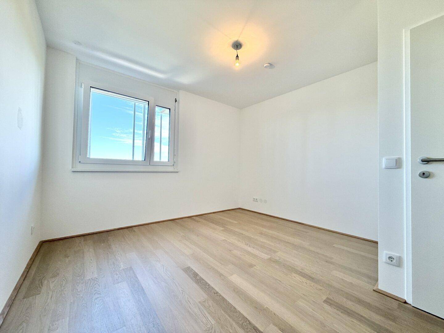 Freundliches Schlafzimmer mit hellem Parkettboden und einem Fenster für natürliche Belichtung.