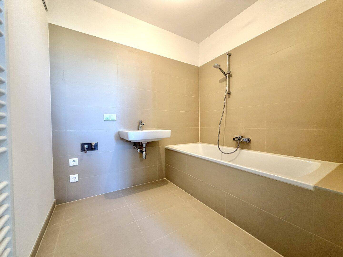 Modernes Badezimmer mit beigefarbenen Fliesen, Badewanne mit Duschfunktion und Handtuchheizkörper.