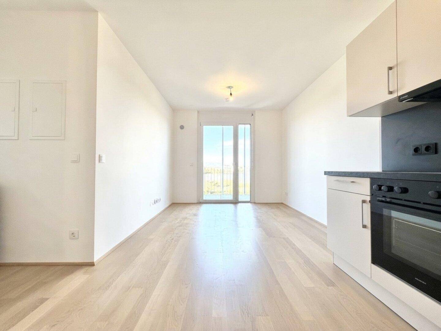 Heller Wohnbereich mit hellem Parkettboden und Zugang zu einem Balkon oder einer Terrasse.