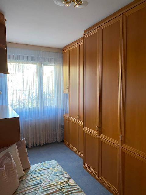 Schlafzimmer mit durchgehenden Einbauschränken aus Holz und einem Fenster mit Vorhängen.