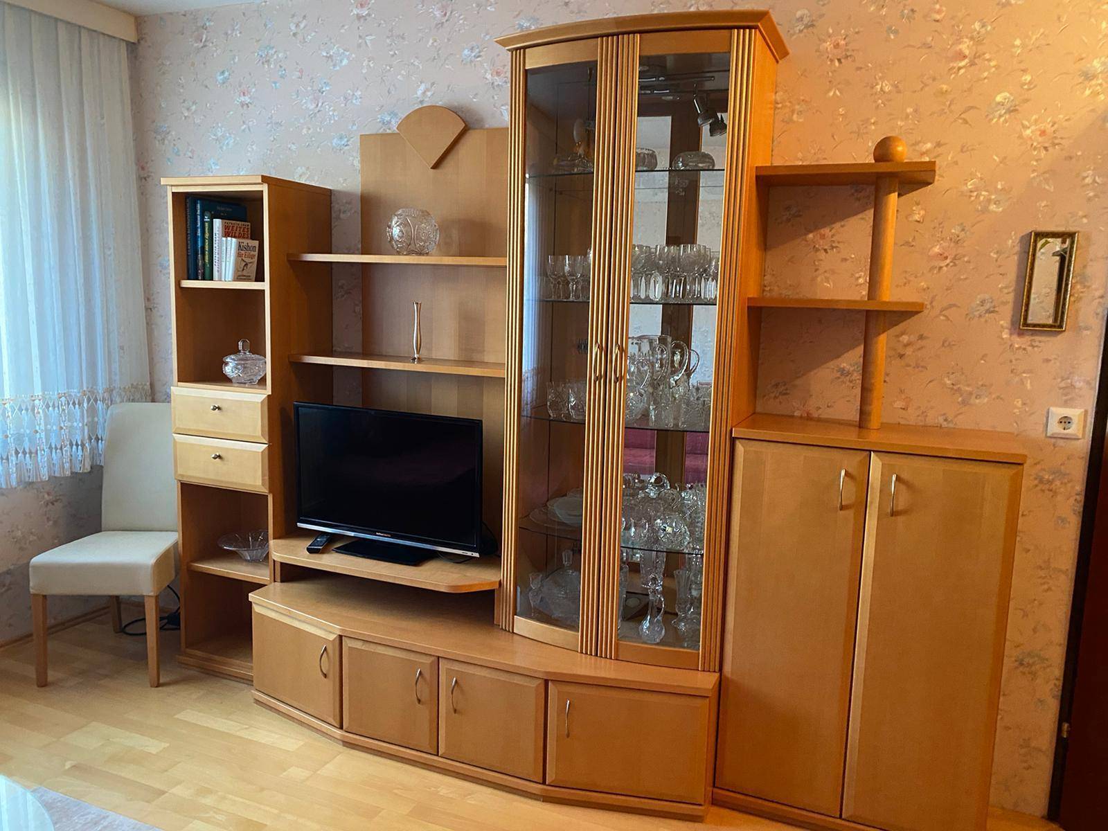Klassische Wohnwand aus hellem Holz mit Vitrine, Fernseher und dekorativen Elementen.