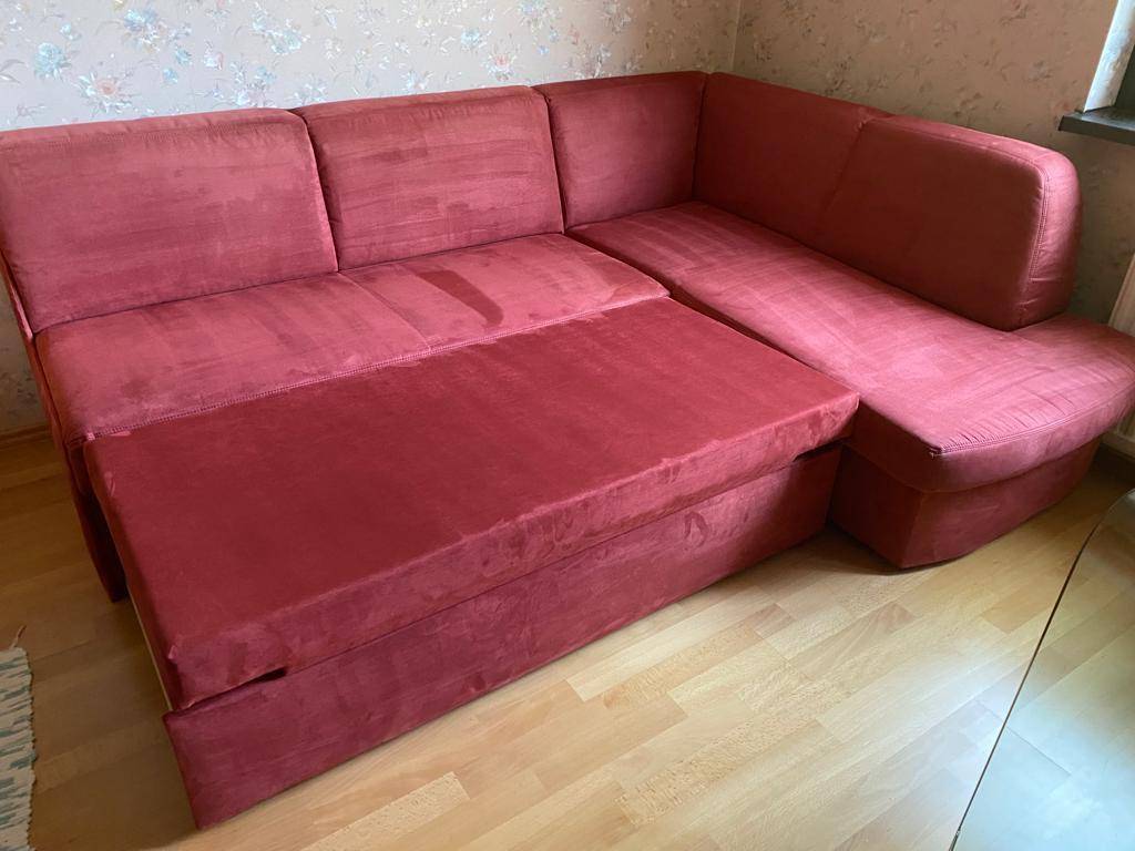 Rotes Ecksofa, das zu einem Schlafsofa ausgezogen wurde, auf hellem Parkettboden.