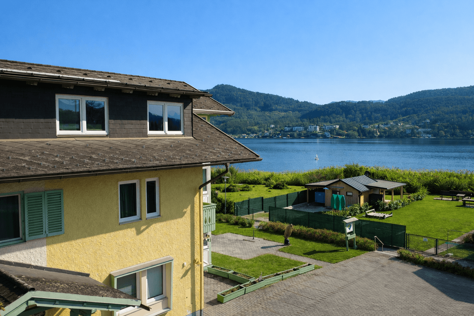 Gelbes Gebäude mit grünen Fensterläden und Blick auf den See und die umliegende Naturlandschaft.