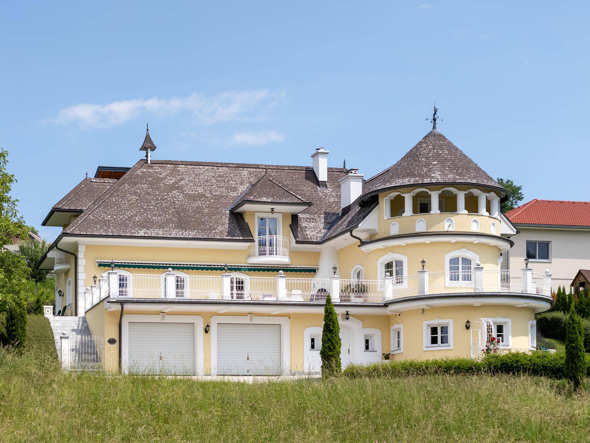 Ansicht der Villa mit markantem Turm, Balkonen und integrierter Doppelgarage im Erdgeschoss.