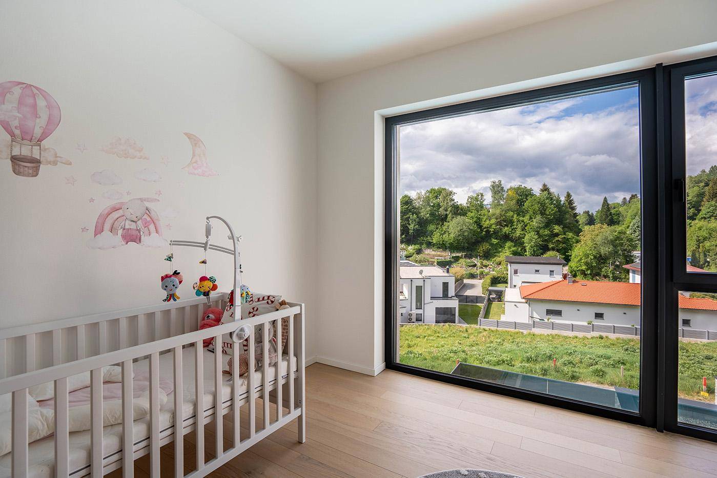 Kinderzimmer mit Babybett und großen Fenstern, die einen weiten Blick in die Natur bieten.