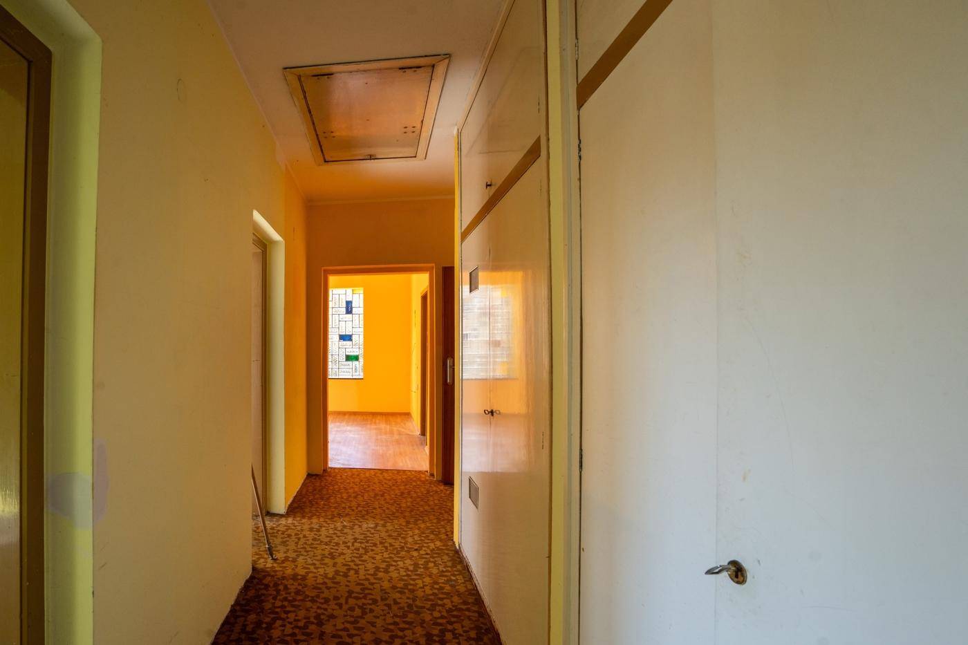 Flur mit Teppichboden und Einbauschränken, der den Blick in ein weiteres Zimmer freigibt.