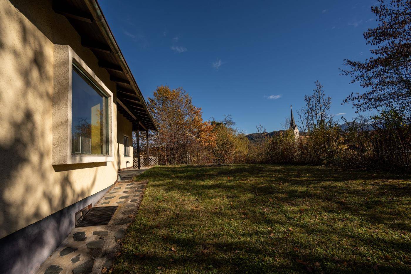 Seitenansicht des Hauses mit einem Steinweg und Blick auf die Kirche und Berge in der Ferne.