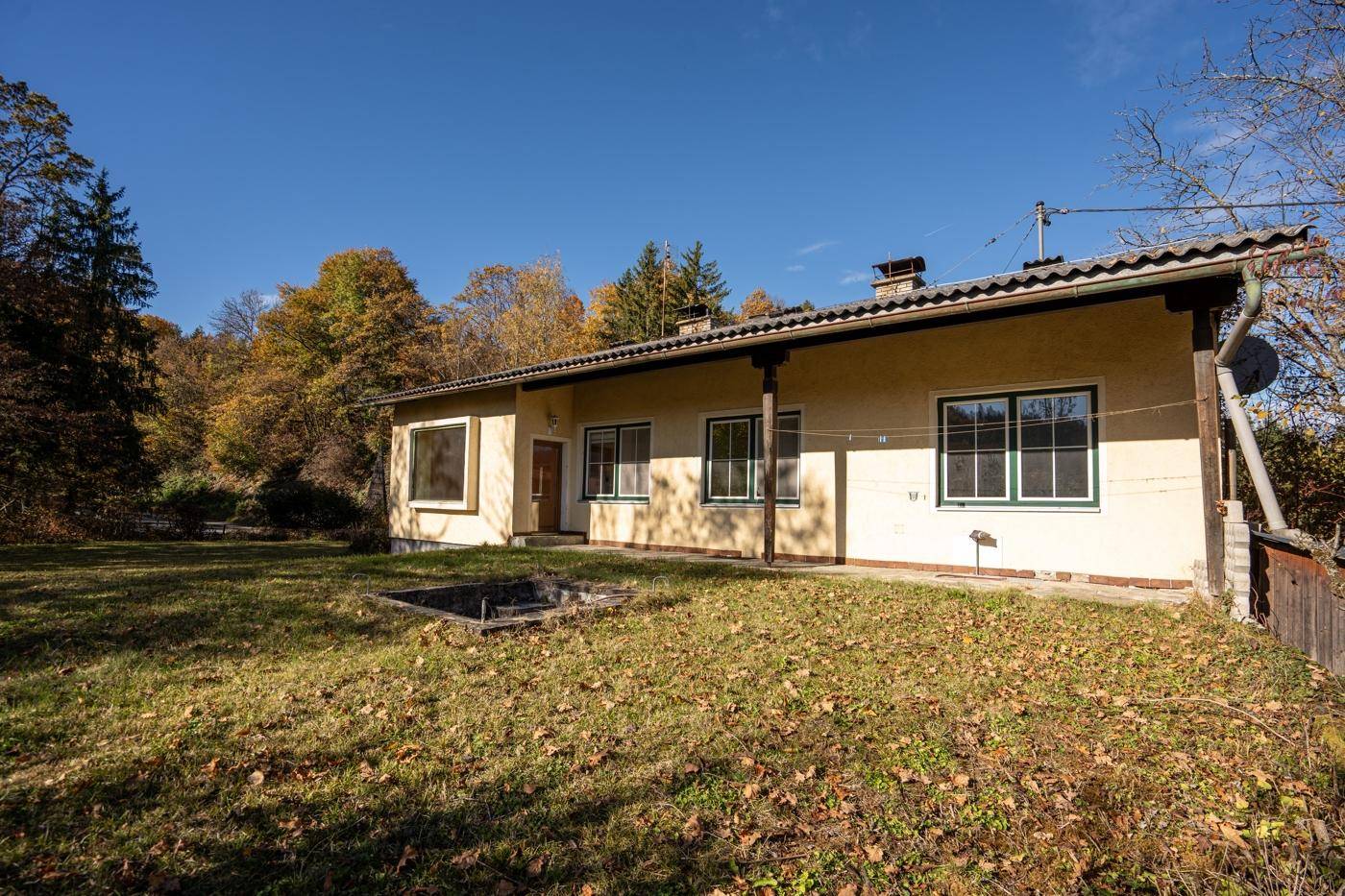 Einfamilienhaus mit gelber Fassade und grünen Fensterläden, umgeben von einem Rasen.