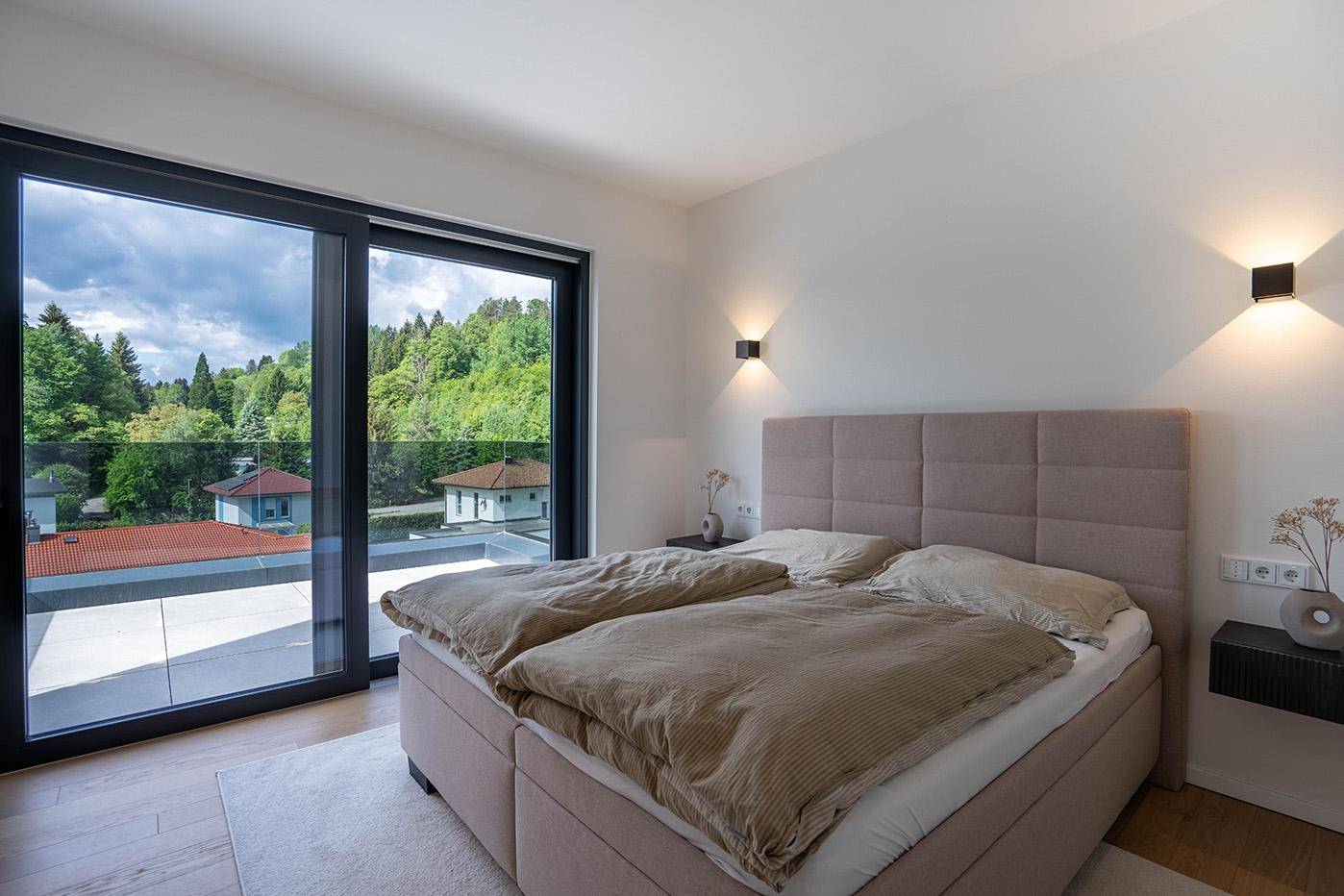 Helles Schlafzimmer mit großem Doppelbett und bodentiefen Fenstern mit Blick ins Grüne.
