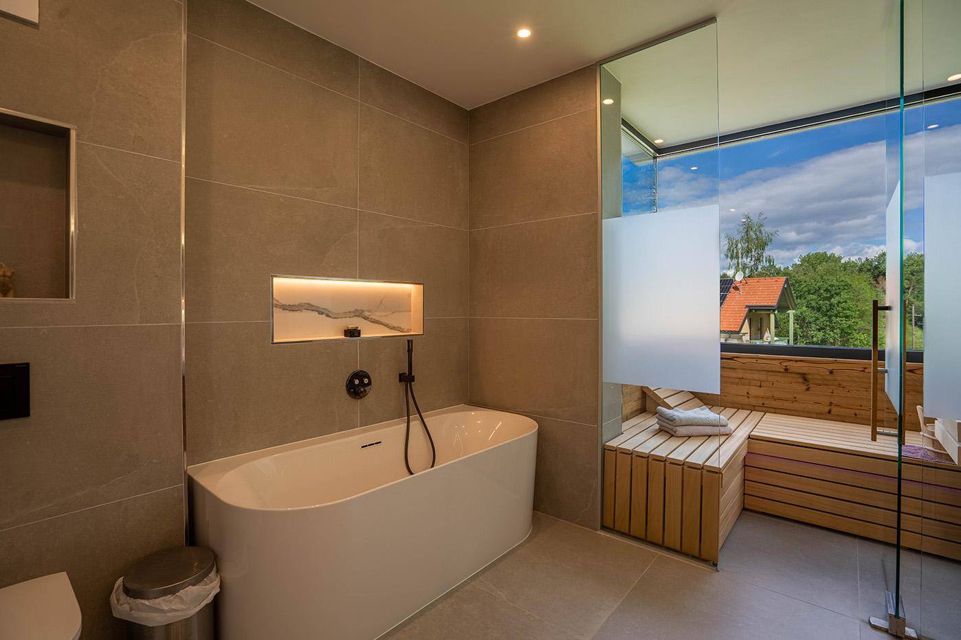 Elegantes Badezimmer mit freistehender Badewanne und direktem Zugang zur Sauna mit Panoramablick.