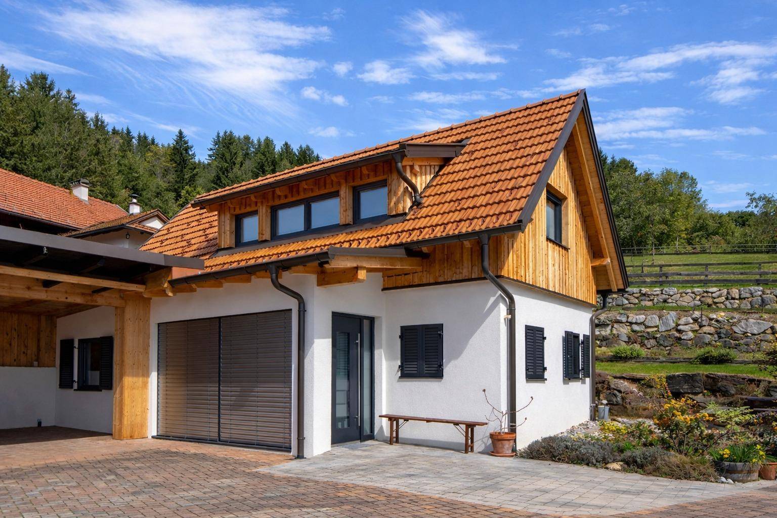 Modernisiertes Gebäude mit weißer Fassade, Holzgiebel und integrierter Garage sowie einem Carport.