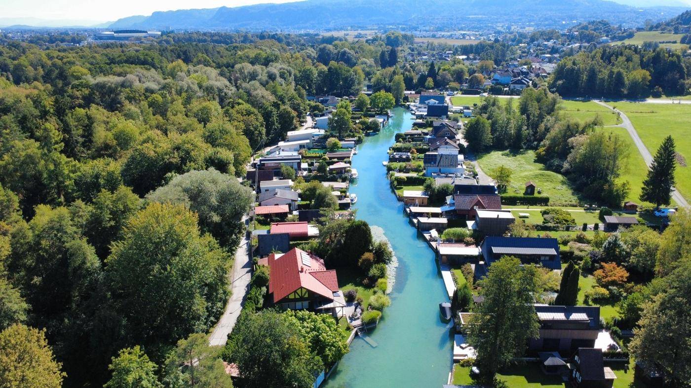 Blick von oben auf eine idyllische Wohngegend mit Häusern direkt am Ufer eines schmalen Wasserlaufs.