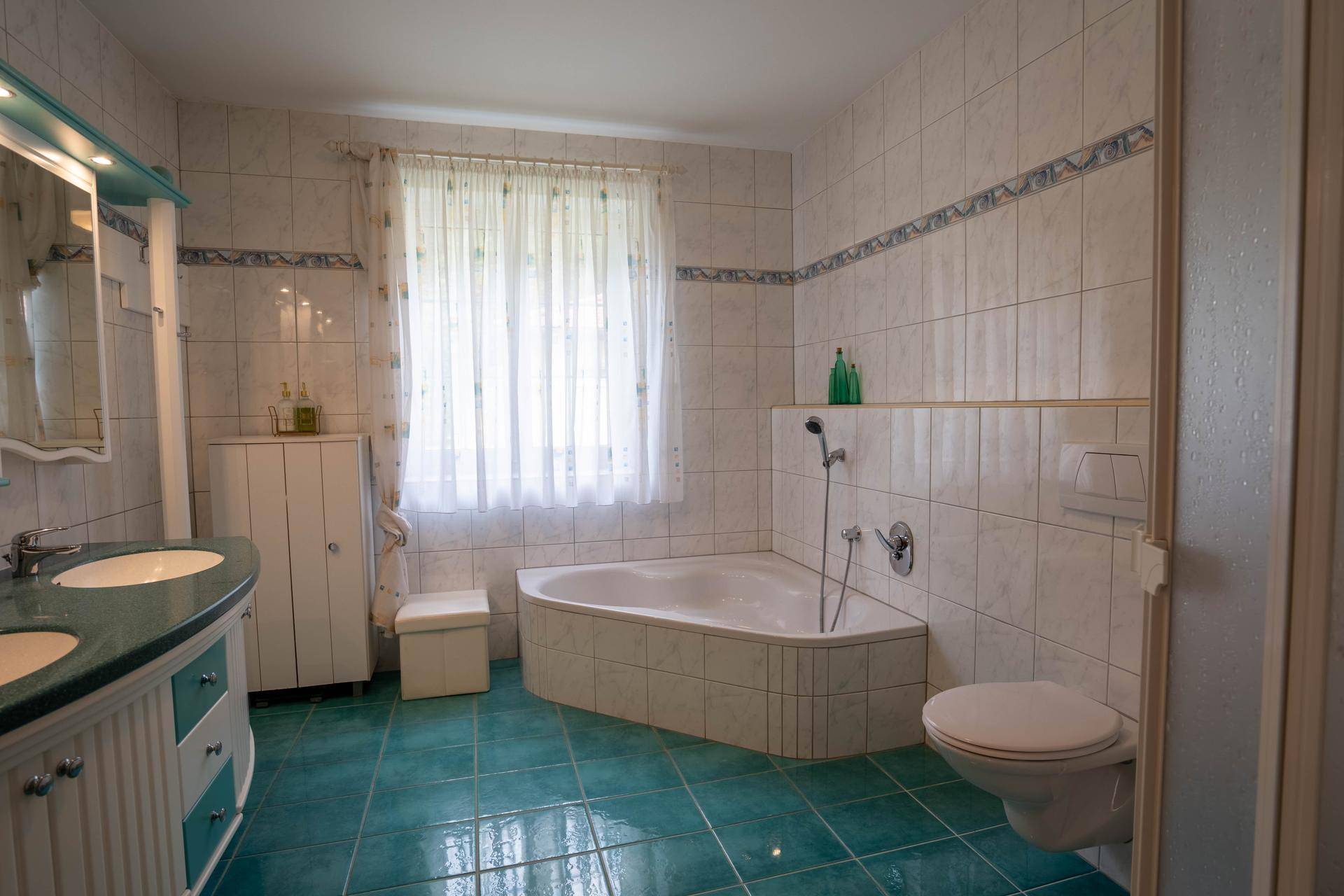 Helles Badezimmer mit Eckbadewanne, Doppelwaschbecken und blauen Fliesen, funktional und gepflegt.