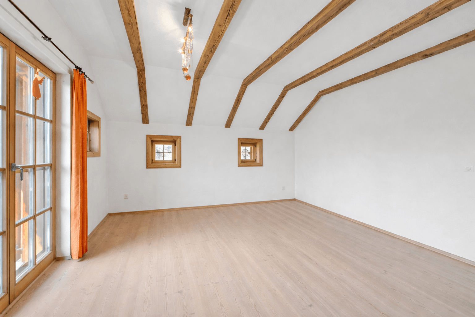 Helles Schlafzimmer mit Holzbalken, Dachschräge und Zugang zu einem Balkon mit traditionellem Geländer.