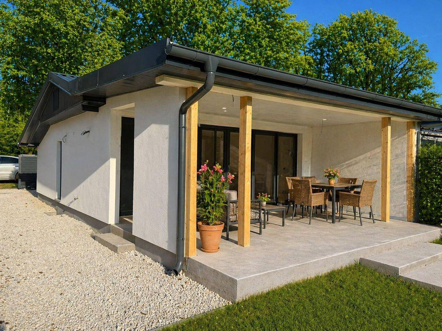 Überdachte Terrasse mit Holzsäulen und stilvollen Gartenmöbeln, umgeben von Grünflächen.