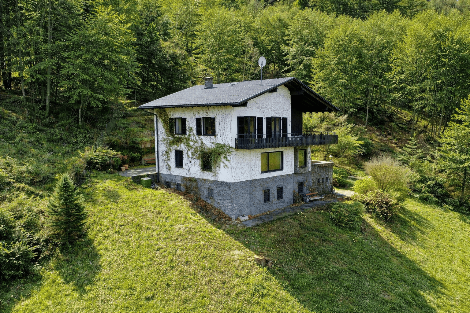 Idyllisches Haus am Hang mit Blick auf die bewaldete Umgebung und einen kleinen Gartenbereich.