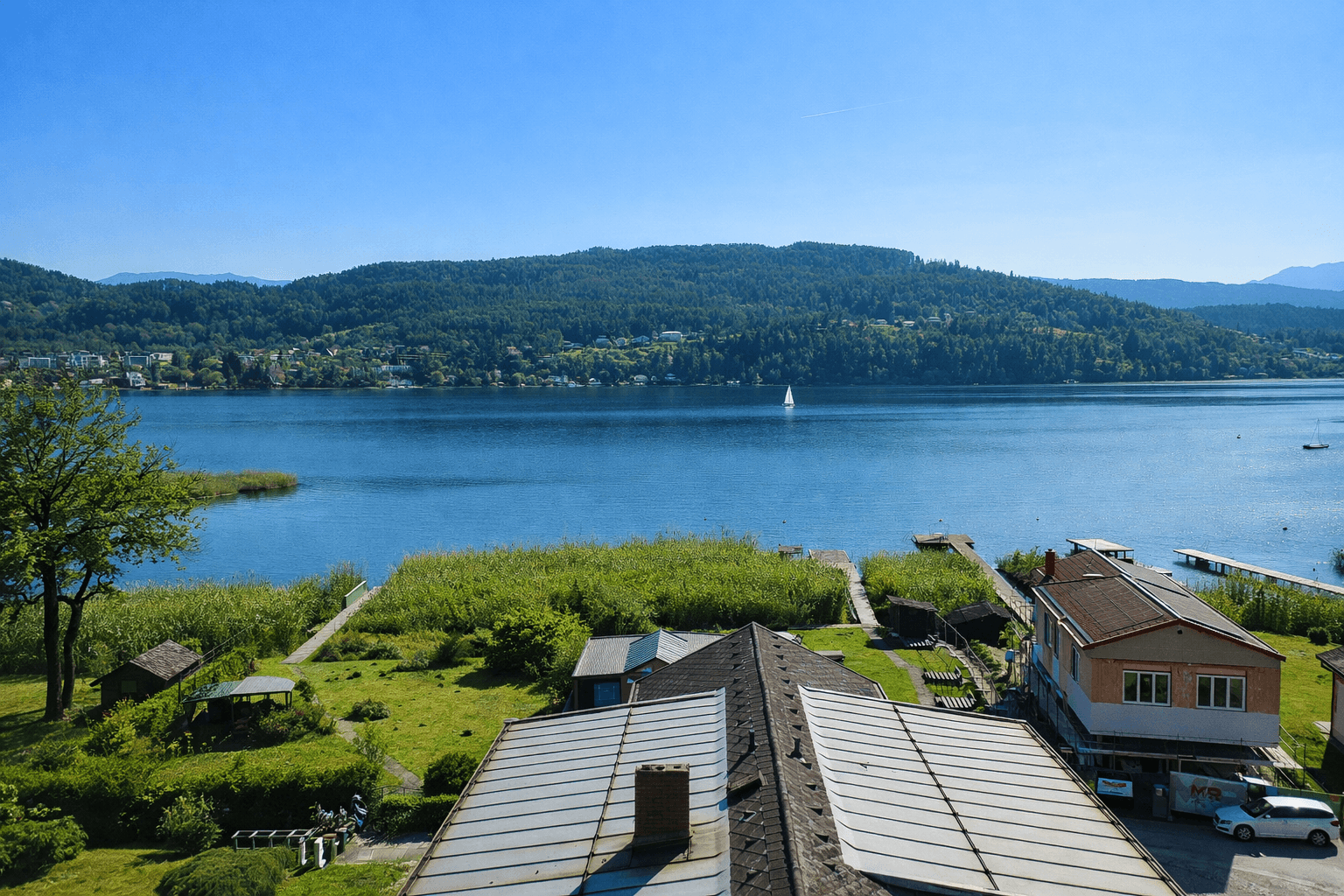 Panoramablick über die Dächer der Gebäude, den See und die bewaldeten Hügel unter klarem Himmel.