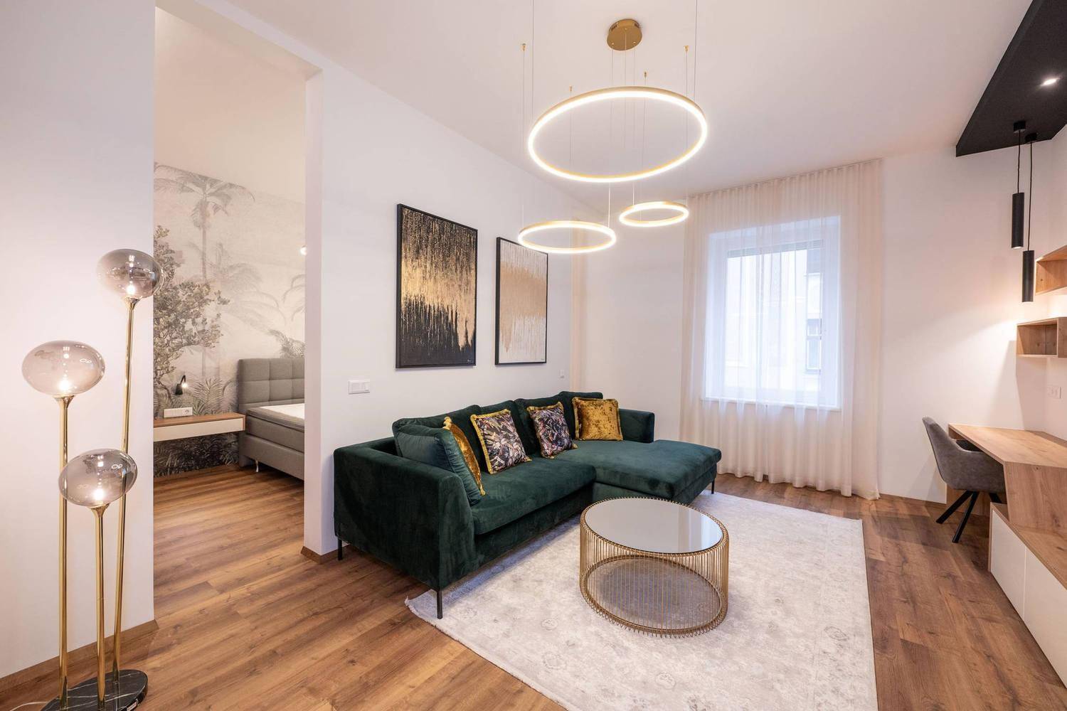 Modernes Wohnzimmer mit dunklem Sofa, Holzboden und offener Verbindung zum Schlafbereich.