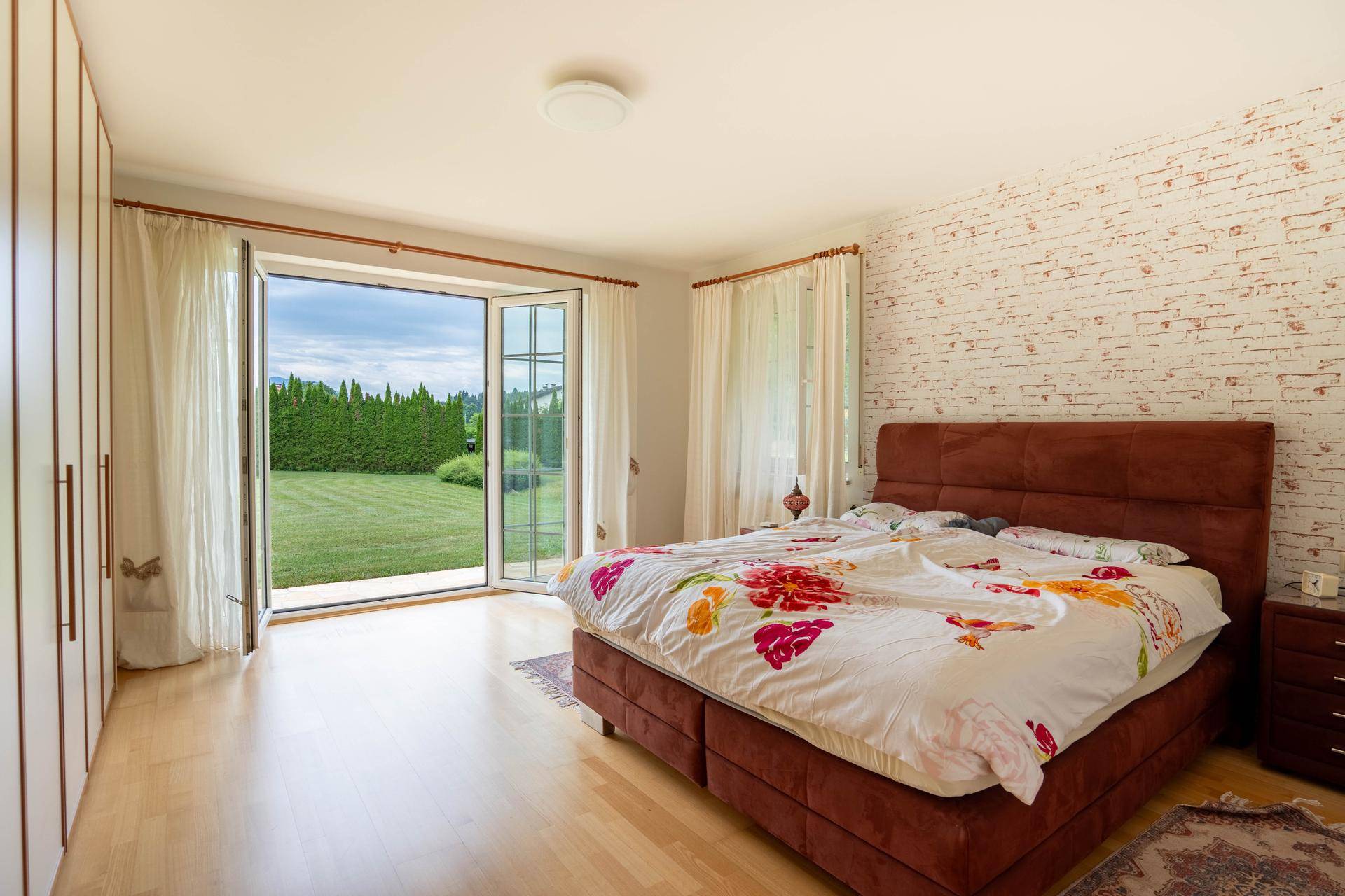 Geräumiges Schlafzimmer mit Holzboden und direktem Zugang zum grünen Gartenbereich.
