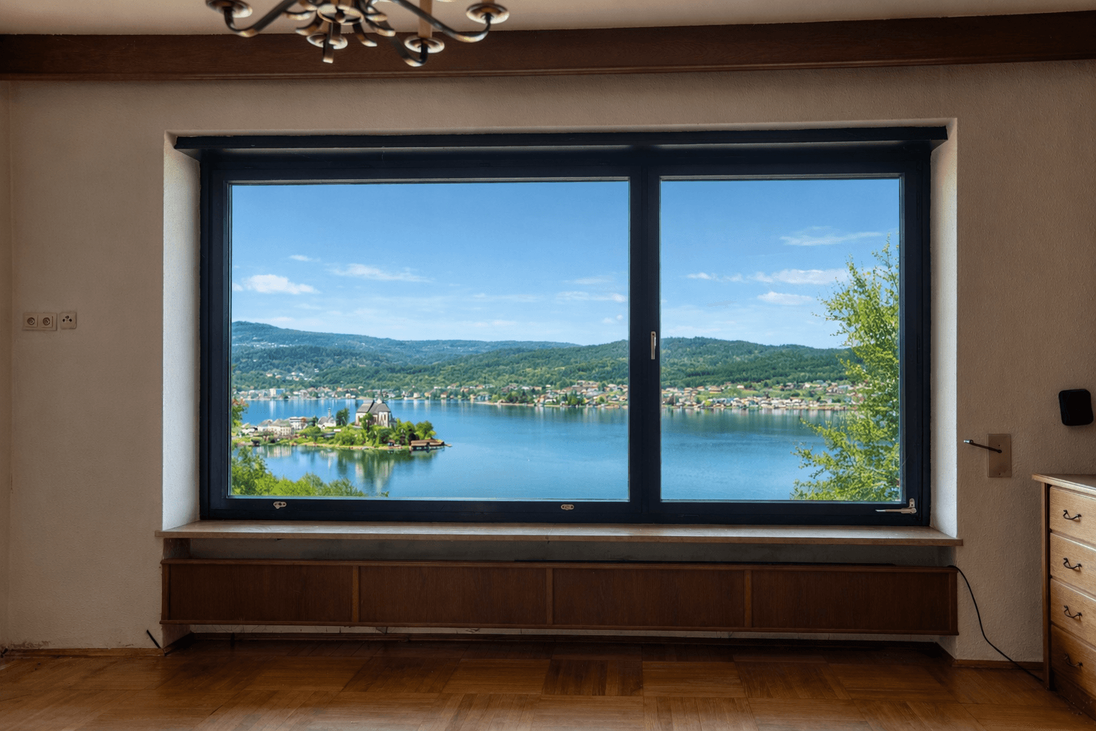 Helles Wohnzimmer mit großem Fenster, das einen atemberaubenden Blick auf den See und die umliegende Landschaft bietet.