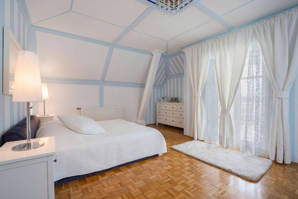 Helles Schlafzimmer mit Holzboden, blauen Streifenwänden und großen Fenstern.