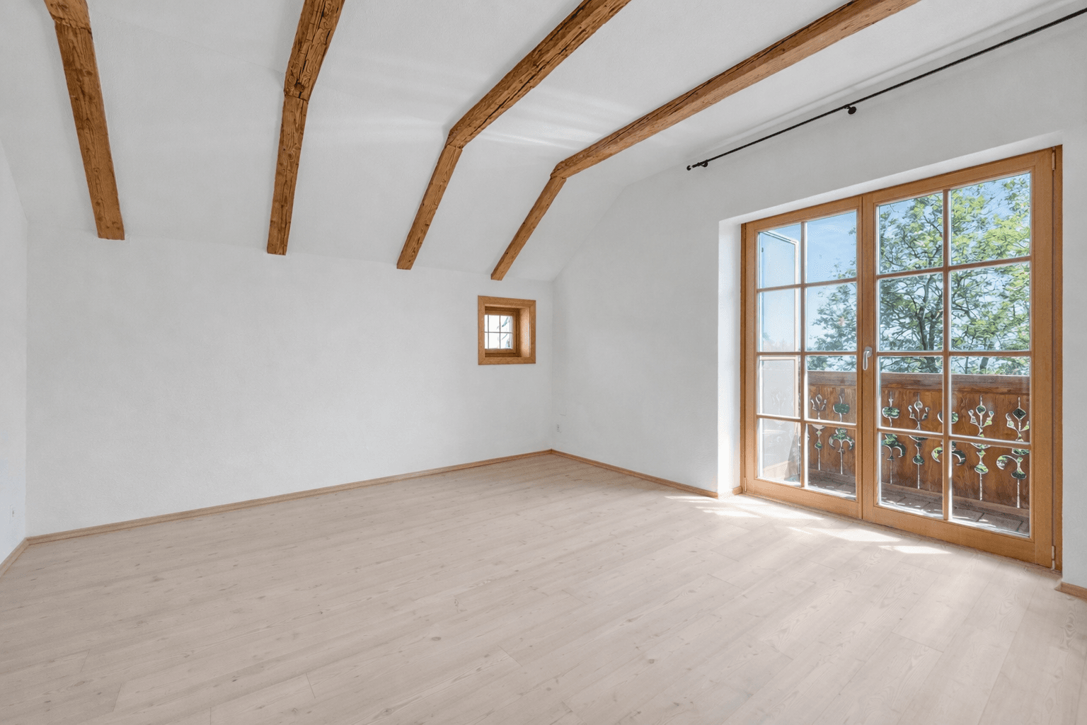 Geräumiges Schlafzimmer mit Holzbalken, Dachschräge und großem Fenster mit Zugang zu einem Balkon.