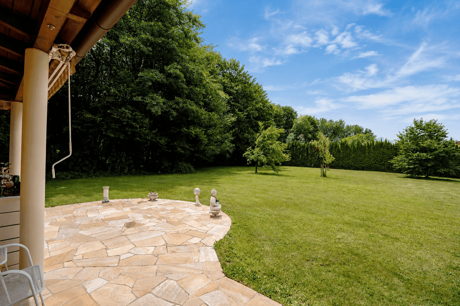 Gepflasterte Terrasse mit Natursteinplatten und weitem Blick in den grünen Gartenbereich.