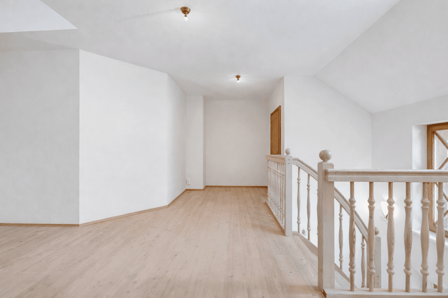 Heller Flurbereich im Obergeschoss mit Holzgeländer, Dachschräge und hellem Holzboden.