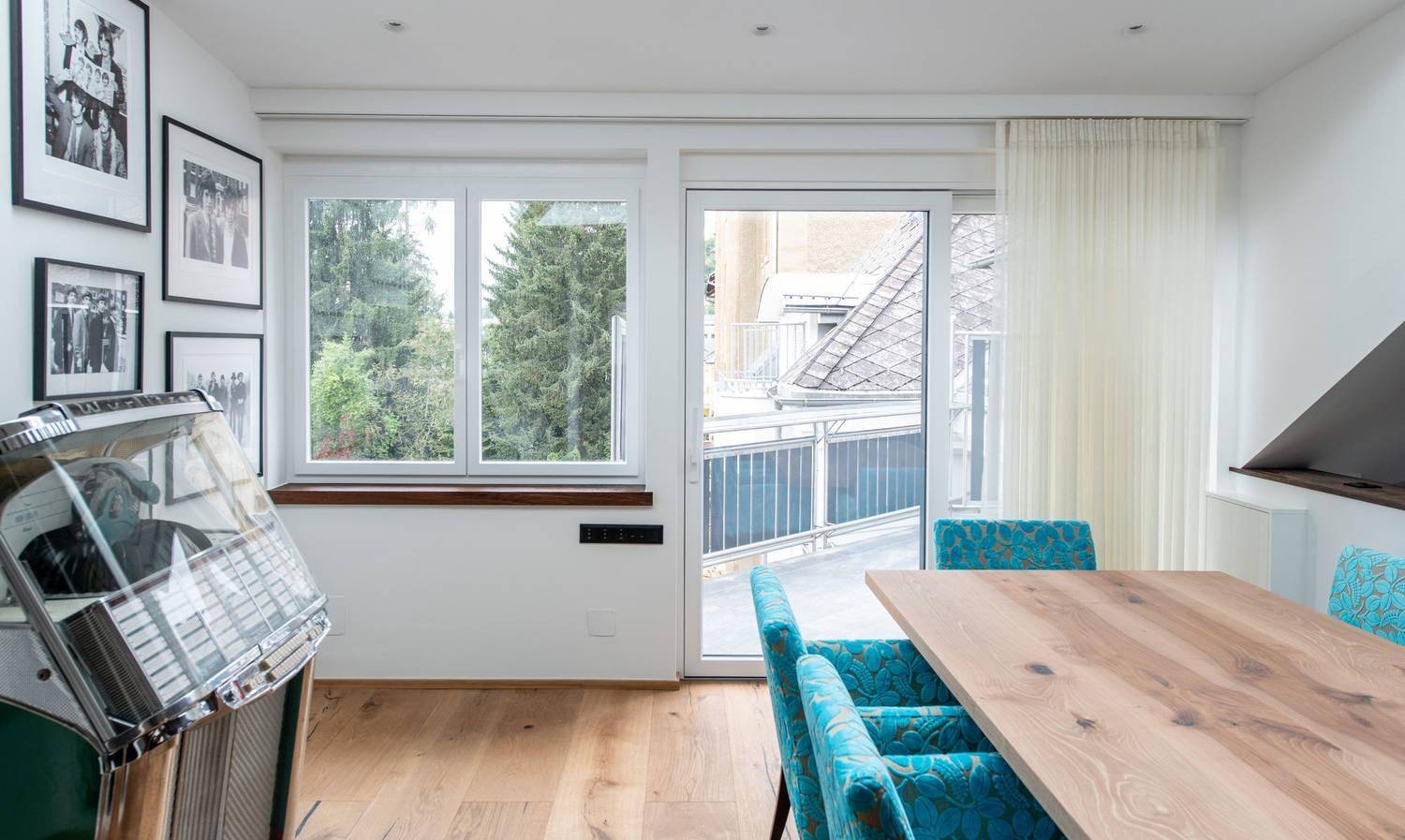 Heller Essbereich mit Holzboden, Blick ins Grüne und Zugang zu einem Balkon.