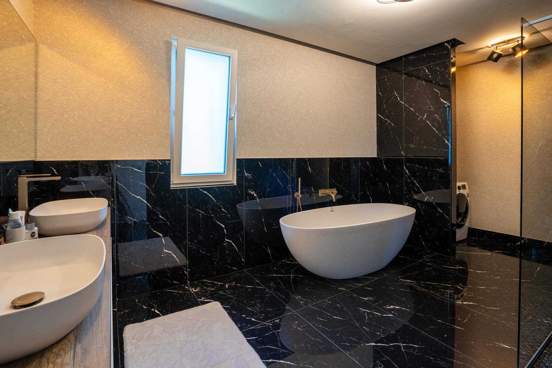 Elegantes Badezimmer mit schwarzem Marmor, freistehender Badewanne, Doppelwaschbecken und Fenster.