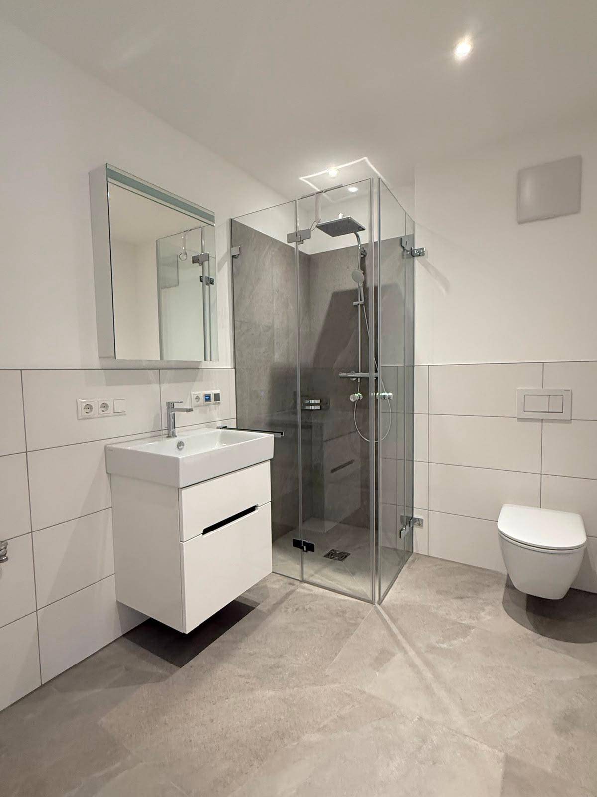 Modernes Badezimmer mit ebenerdiger Glasdusche, Wand-WC und großformatigen grauen Fliesen.