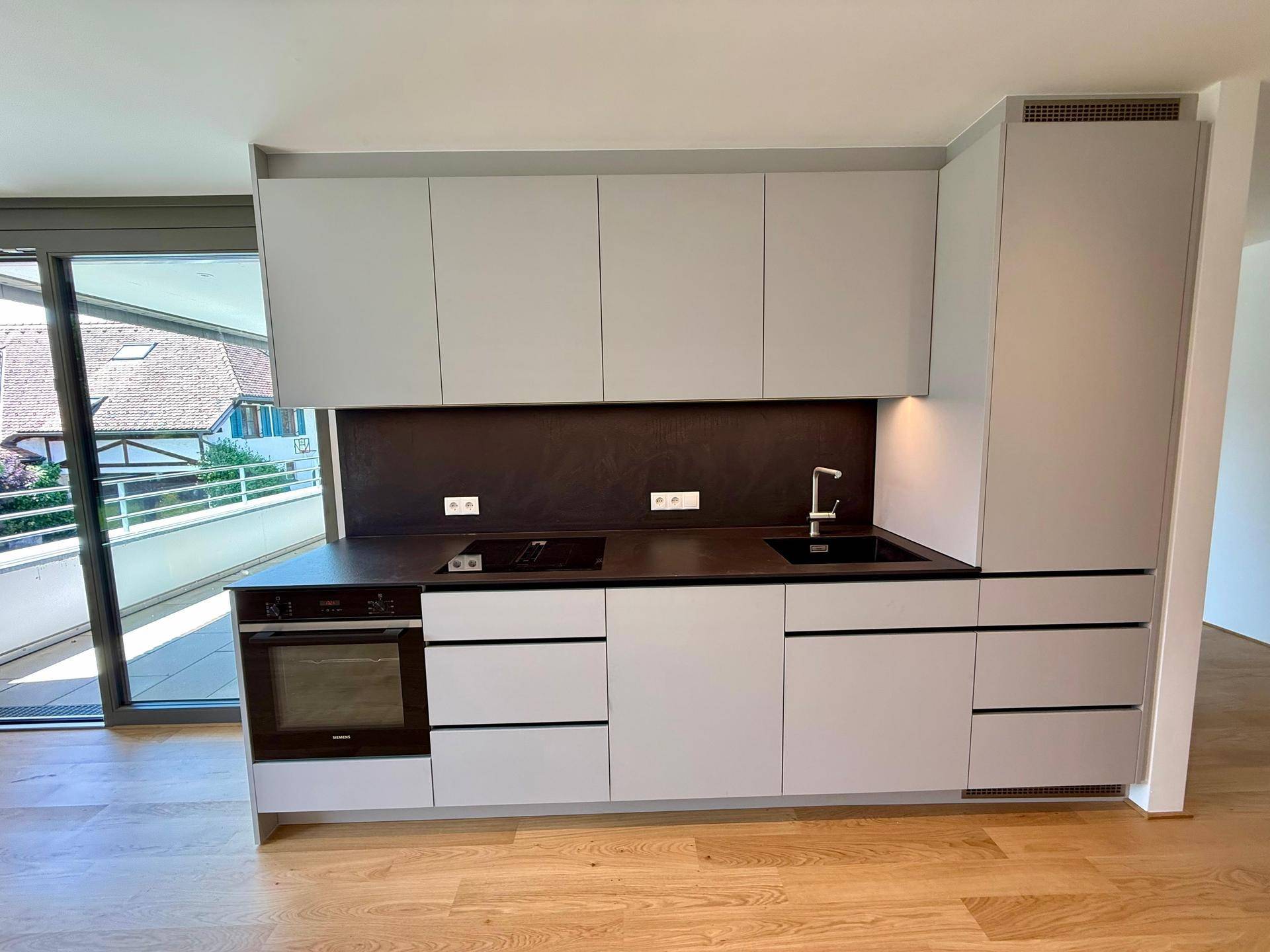 Moderne Einbauküche in hellem Grau mit integrierten Geräten und dunkler Arbeitsplatte.