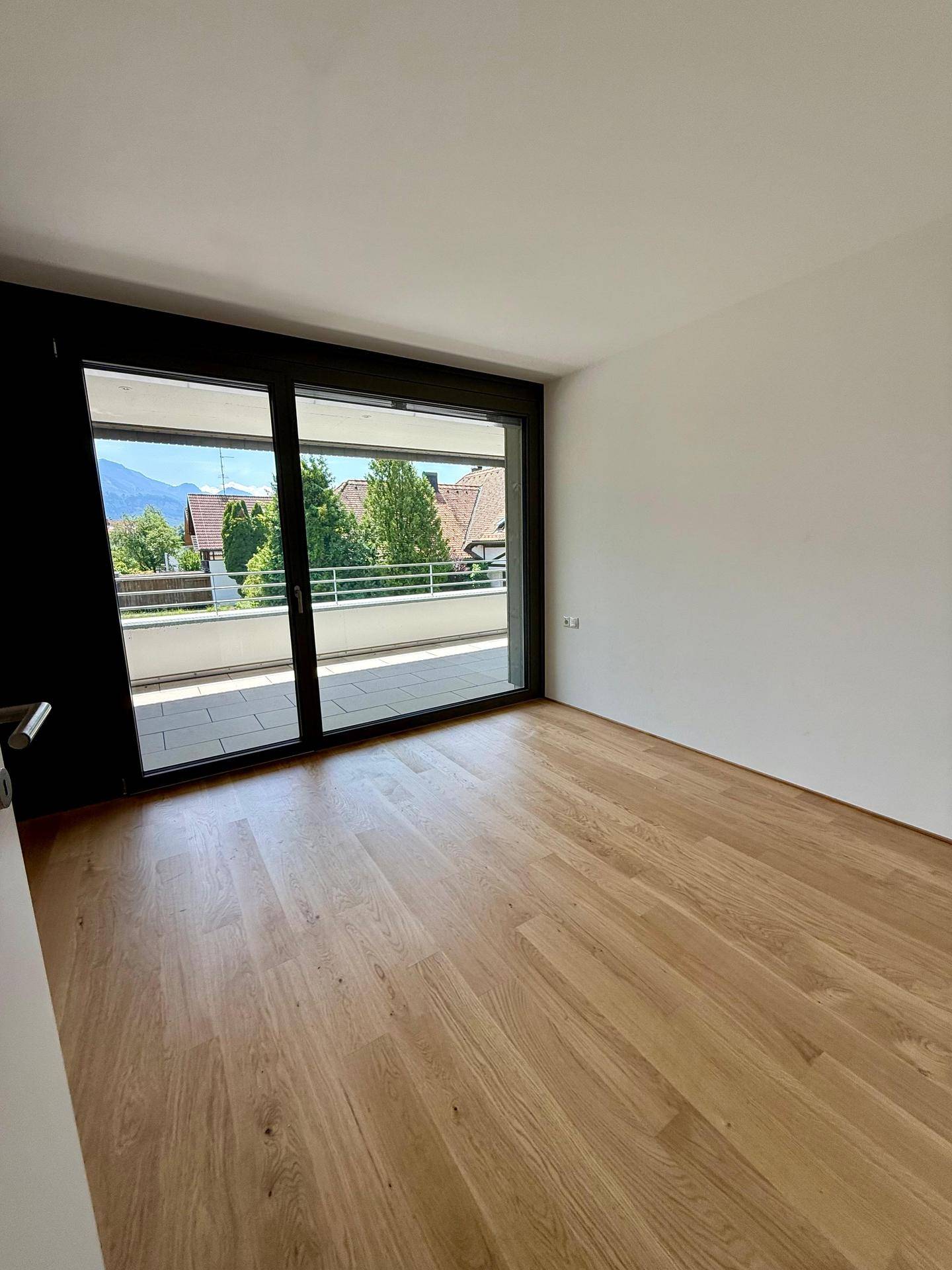 Helles Schlafzimmer mit Holzboden, großen Fenstern und Zugang zum Balkon mit Bergblick.