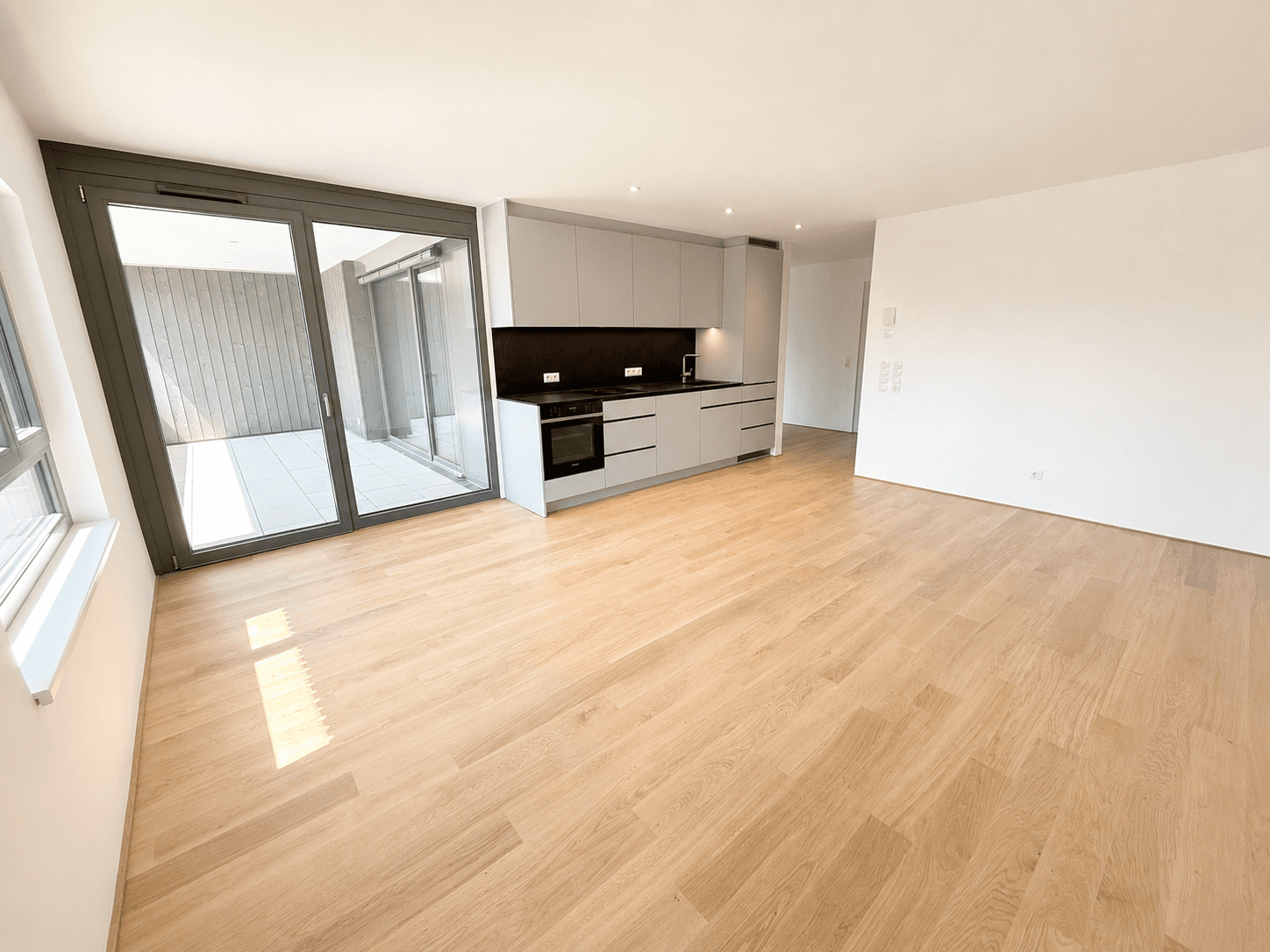 Heller offener Wohnbereich mit integrierter Küche, Holzboden und Zugang zur Terrasse.