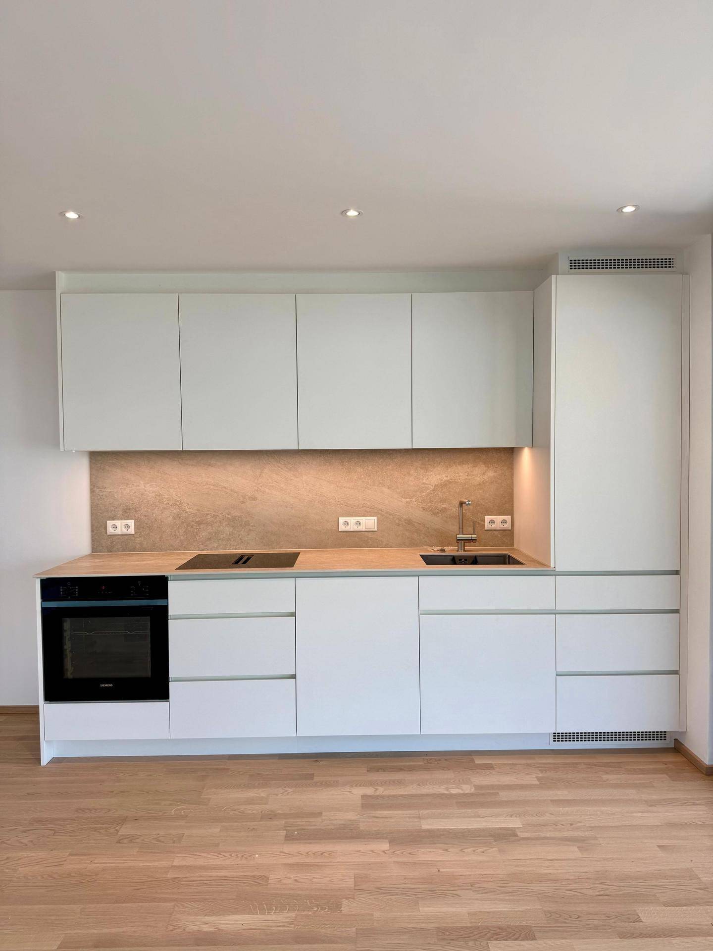 Moderne Einbauküche in Weiß mit Holz-Arbeitsplatte, integrierten Geräten und hellem Parkettboden.