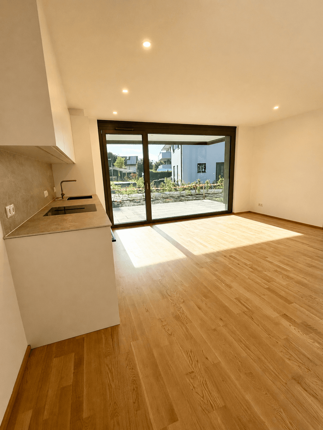 Heller offener Wohnbereich mit Küchenzeile, großen Schiebetüren und Zugang zu einer Terrasse.