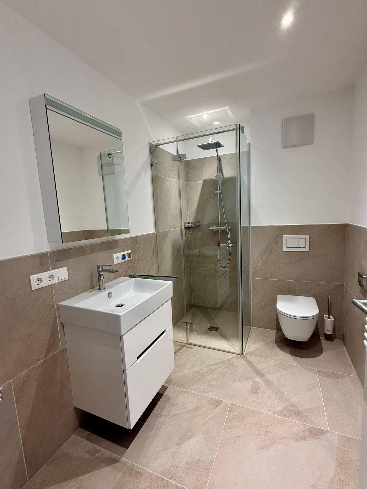 Modernes Badezimmer mit beigefarbenen Fliesen, ebenerdiger Dusche und wandhängendem WC.