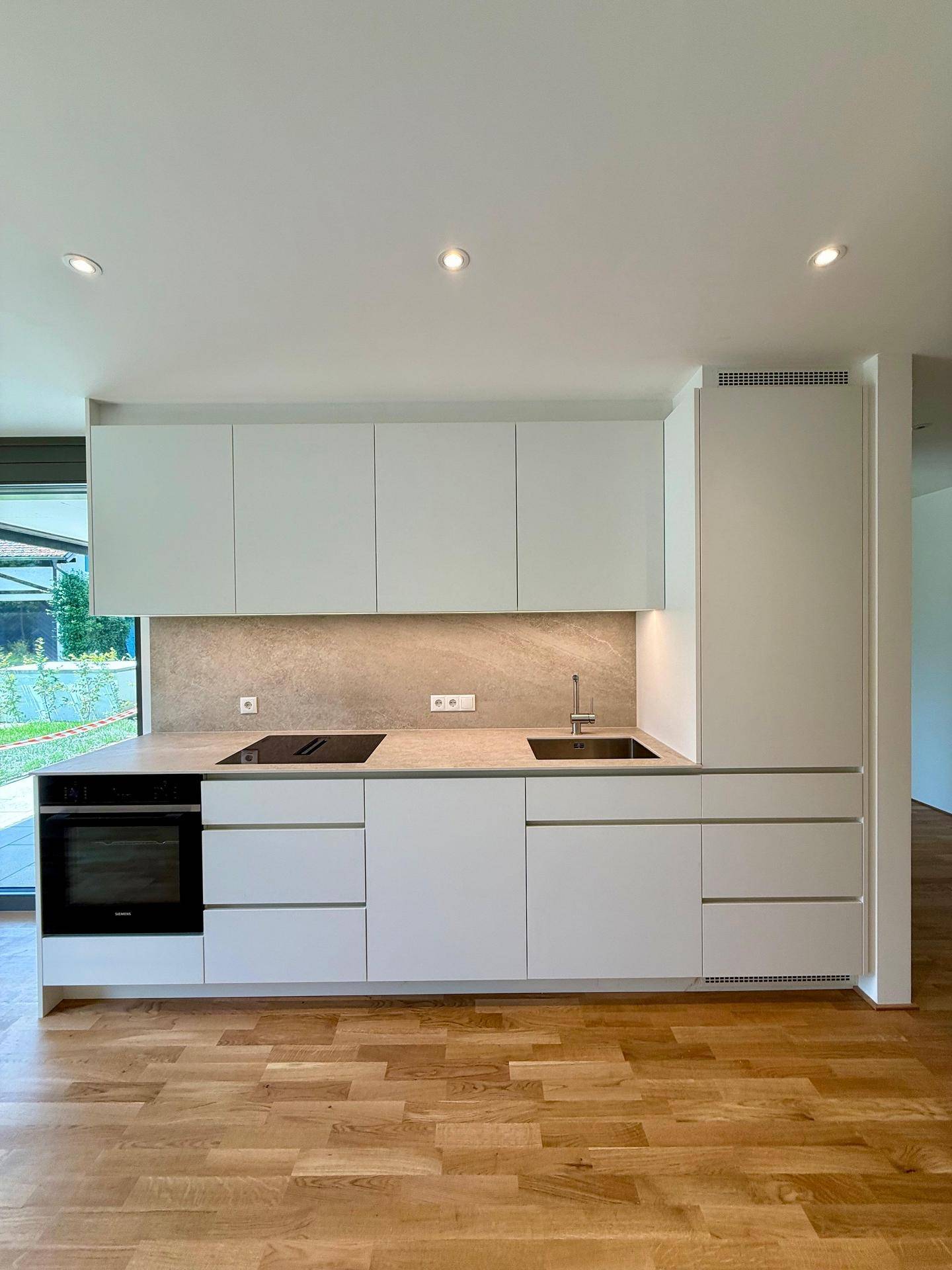 Moderne Einbauküche mit weißen Fronten, Induktionskochfeld und integriertem Backofen.