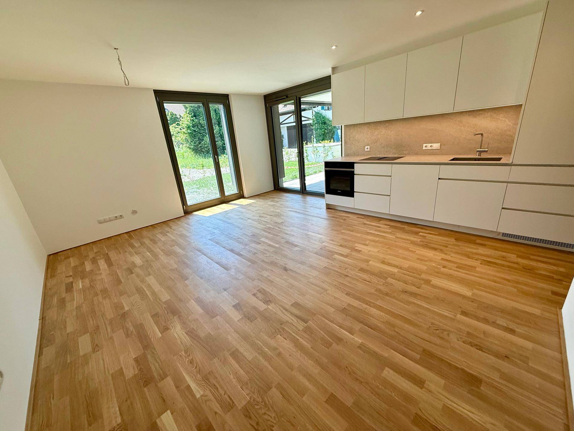Heller offener Wohnbereich mit integrierter Küche, Parkettboden und Zugang zum Garten.